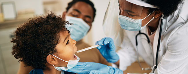 Doctor examing the throat of a young black child